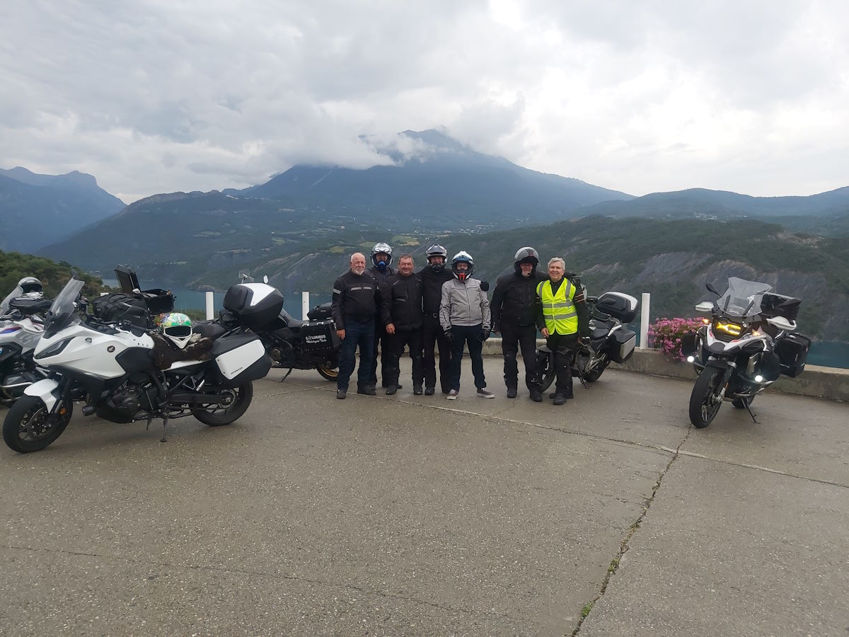 Columbus motorcycle group riders with bikes Lac de Serre-Ponçon mountain backdrop Route Napoleon tour 2024